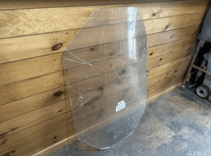 Gehl R & V Series clear polycarbonate windshield panel leaning against wood wall, showing full panel profile