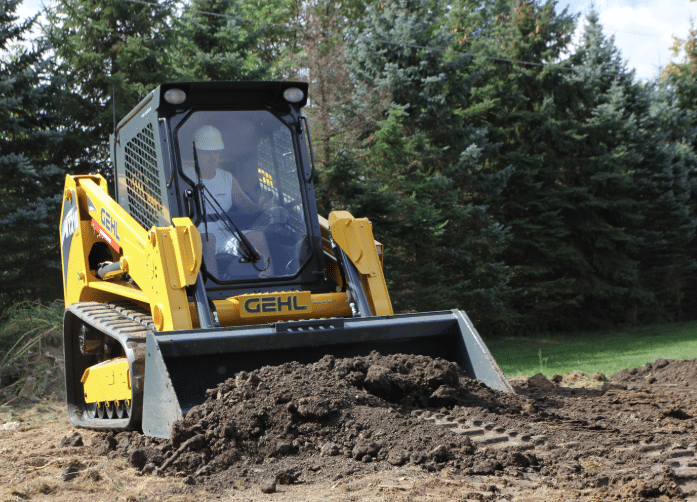 Gehl RT250 compact track loader with operator inside cab moving dirt in a wooded outdoor work site