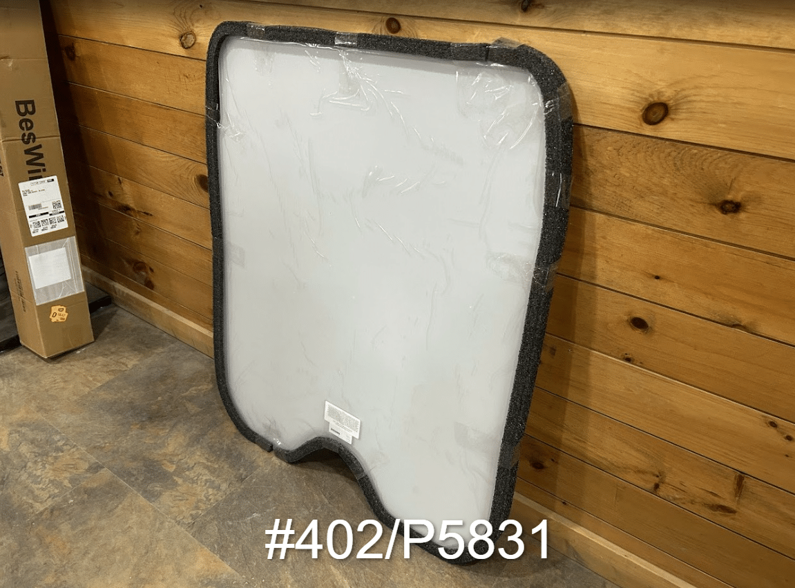 JCB #402/P5831 polycarbonate skid steer front windshield with rubber seal frame leaning against wooden wall, front view