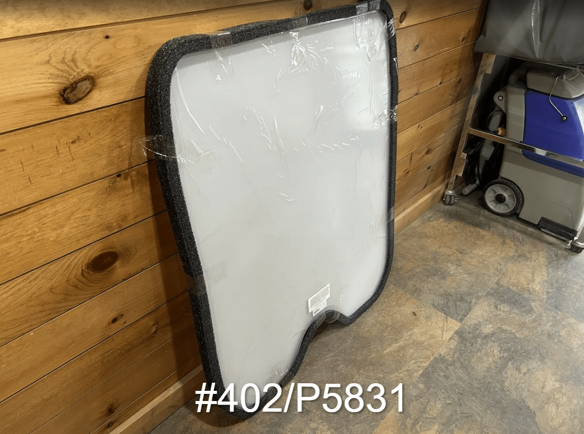 JCB #402/P5831 polycarbonate skid steer windshield with rubber seal shown from a side angle against wooden wall
