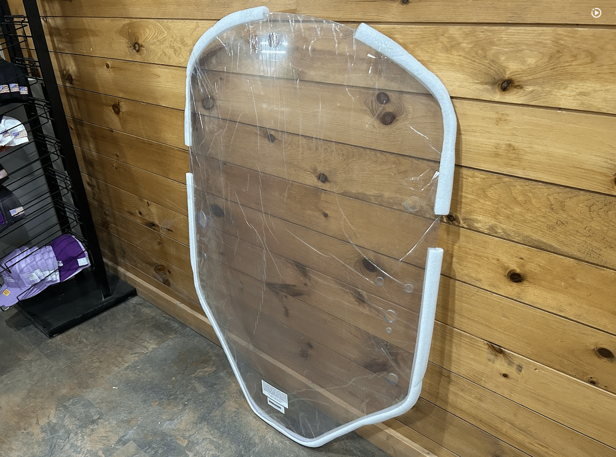 John Deere G Series small frame clear polycarbonate windshield with white frame leaning against wooden wall in shop