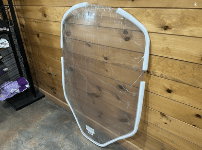 John Deere G Series small frame clear polycarbonate windshield with white frame leaning against wooden wall in shop
