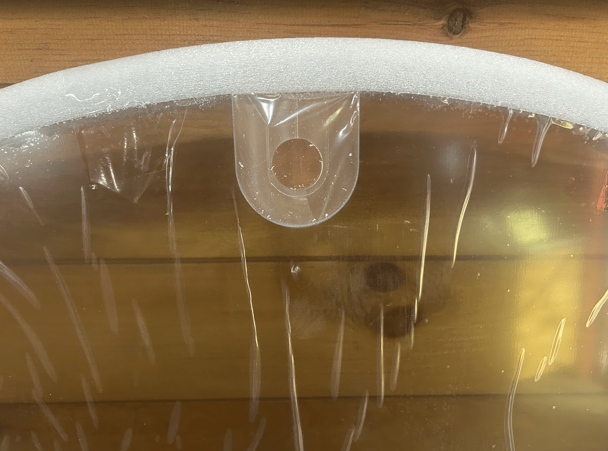 Close-up of top center mounting tab and round hole on John Deere G Series small frame windshield in protective wrap