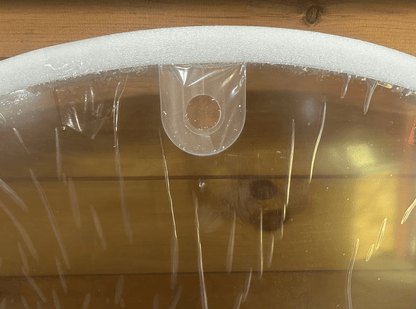 Close-up of top center mounting tab and round hole on John Deere G Series small frame windshield in protective wrap