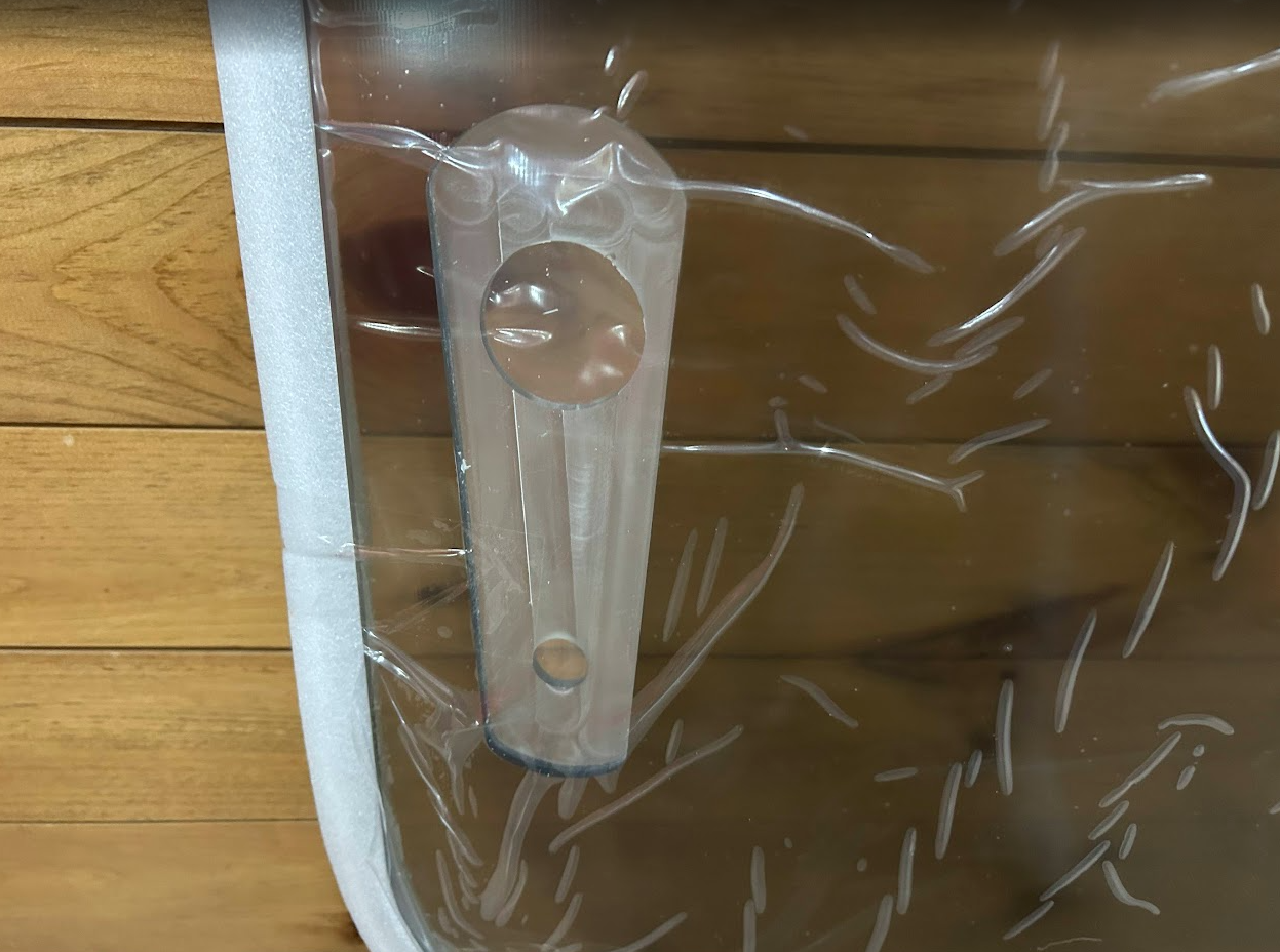 Close-up of John Deere P Series windshield hinge bracket with cylindrical pin slot on foam-padded white frame
