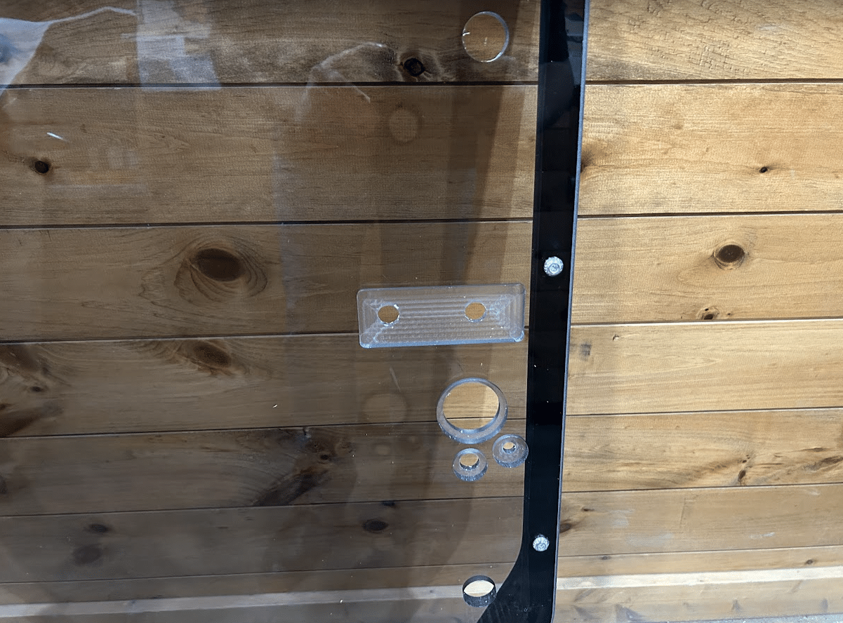 Close-up of tinted John Deere P Series windshield frame right side latch mechanism with catch bracket