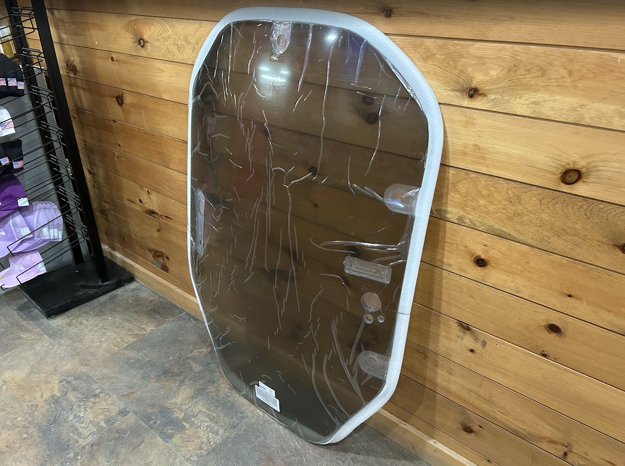 John Deere P Series tinted polycarbonate windshield with white frame leaning in store, mounting brackets on right side
