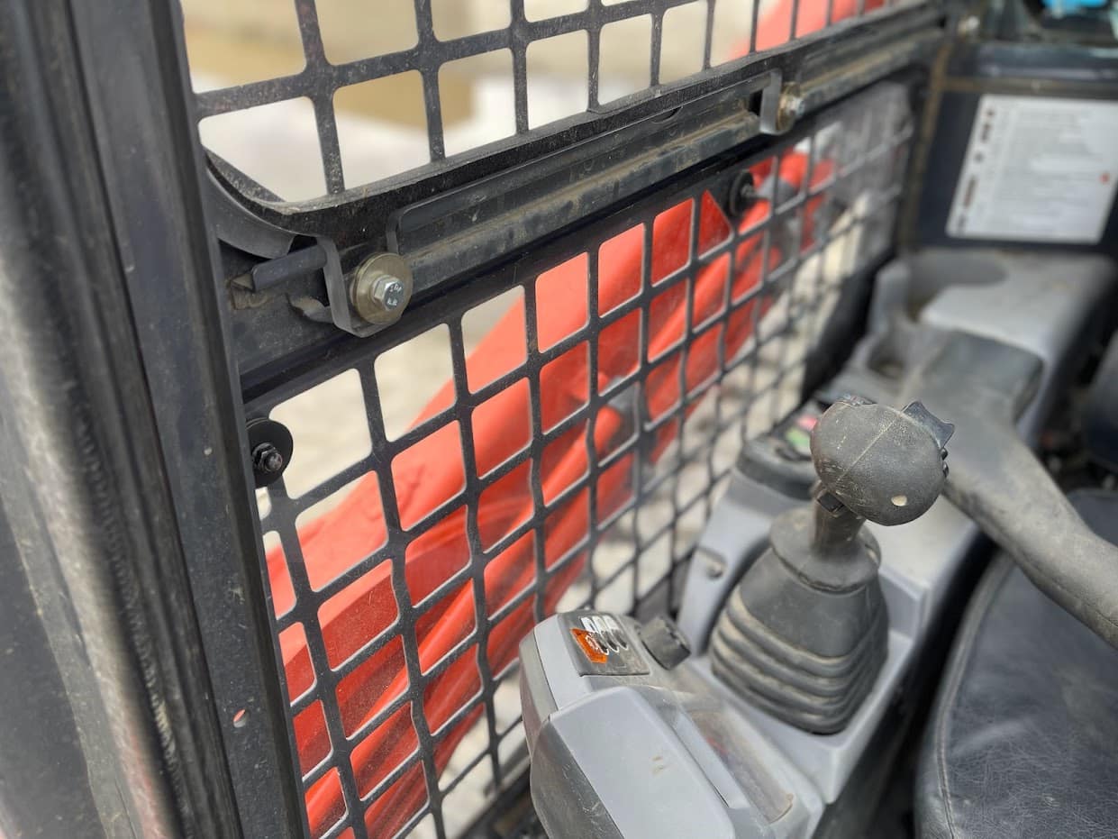 Inside view of Kubota SVL cab showing side window frame with retaining bars and joystick control visible