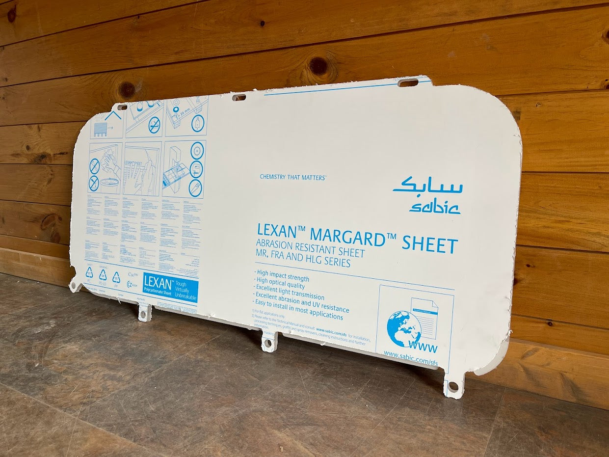 Kubota SVL lower polycarbonate side window panel with Lexan Margard protective film, angled view against wooden background