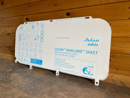 Kubota SVL lower polycarbonate side window panel with Lexan Margard protective film, angled view against wooden background