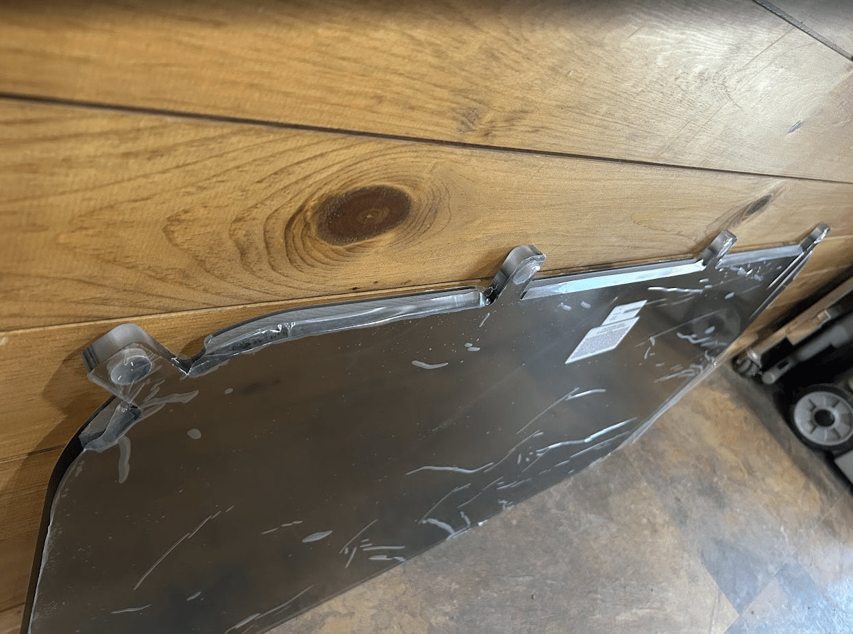 Close-up of corner mounting tab on Kubota SVL tinted polycarbonate side window panel with protective wrap
