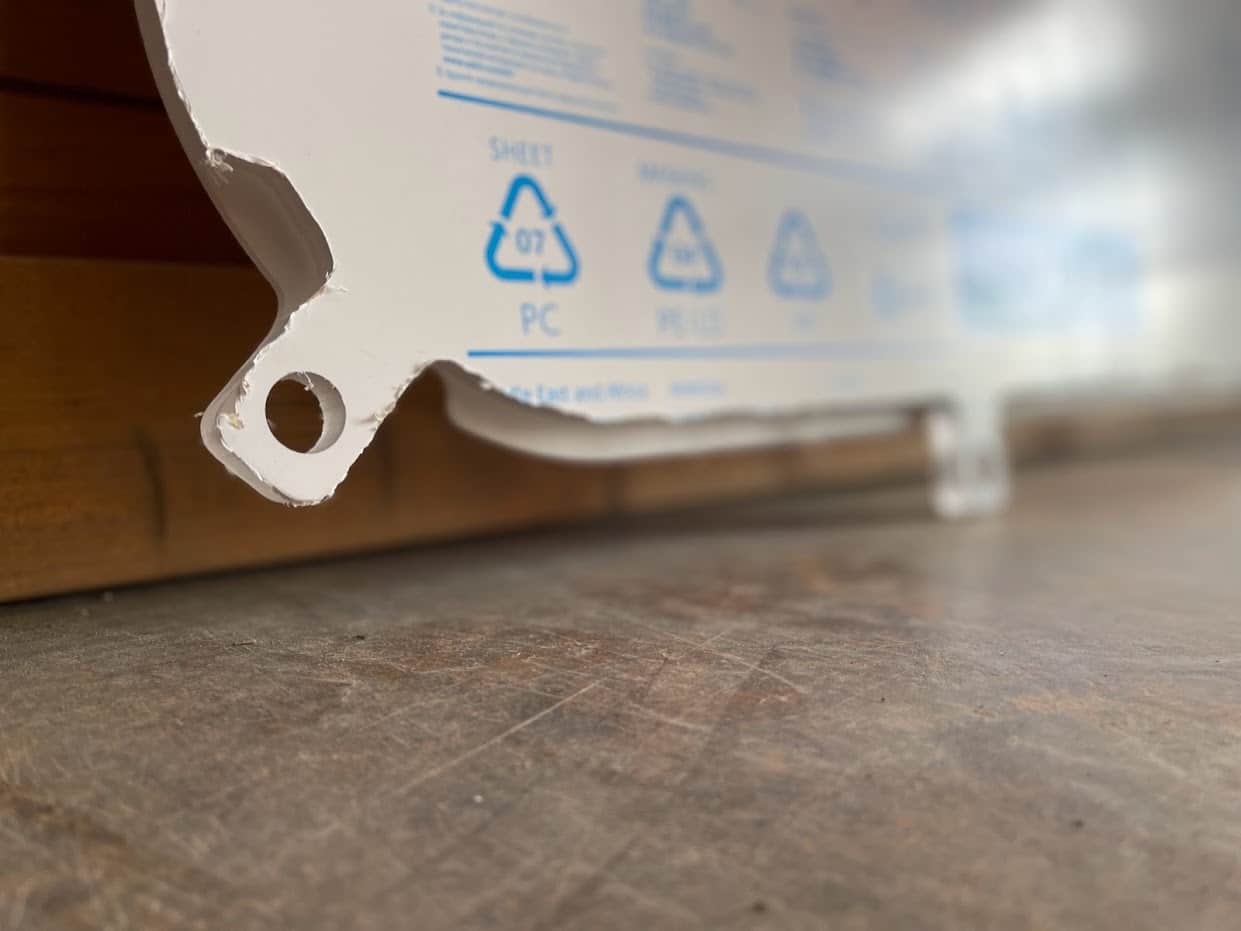 Close-up of polycarbonate side window corner tab with round mounting hole, PC material marking visible on protective film
