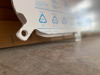 Close-up of polycarbonate side window corner tab with round mounting hole, PC material marking visible on protective film