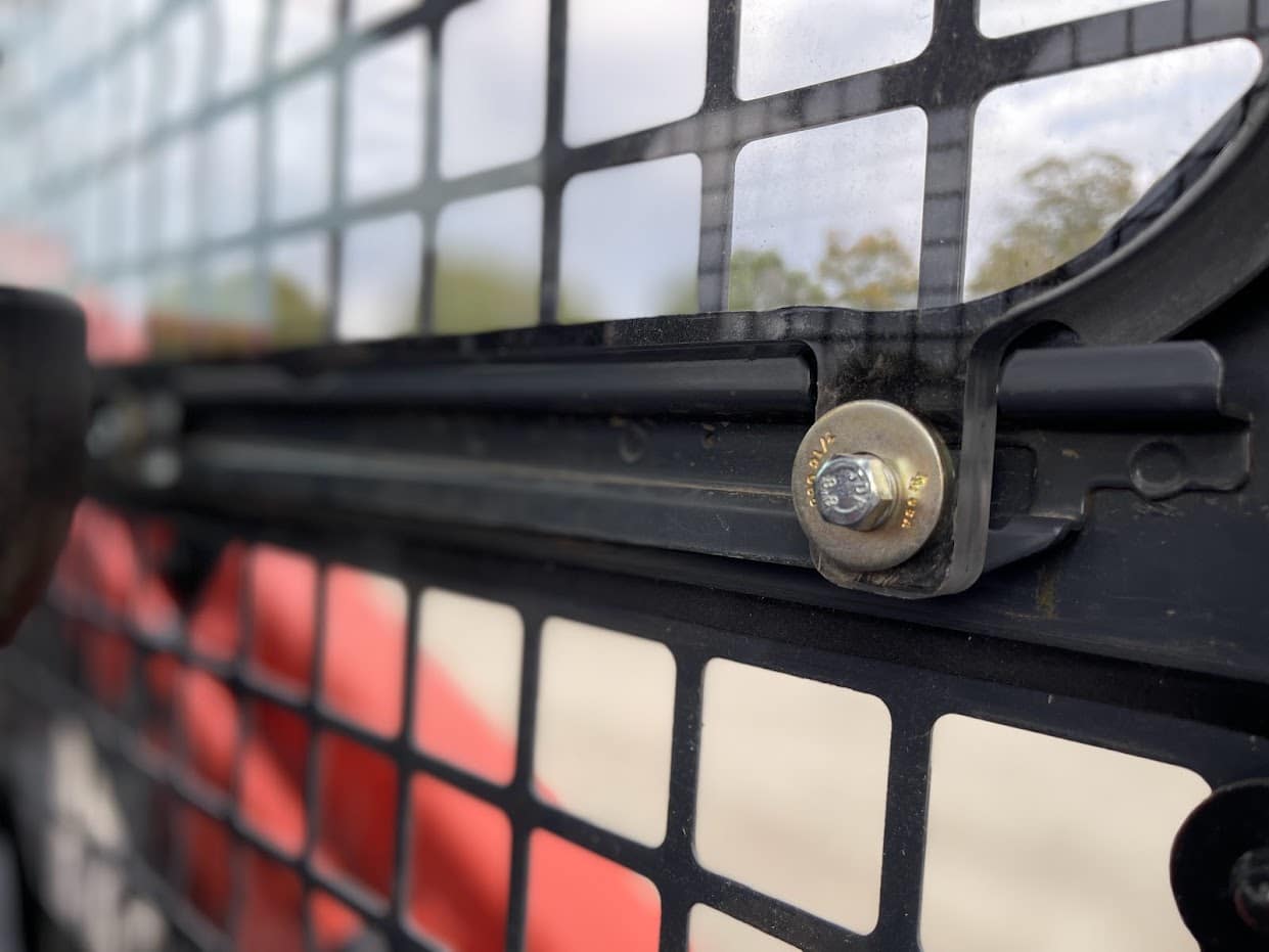 Close-up of bolt and metal retaining hardware securing Kubota SVL polycarbonate side window panel in cab frame