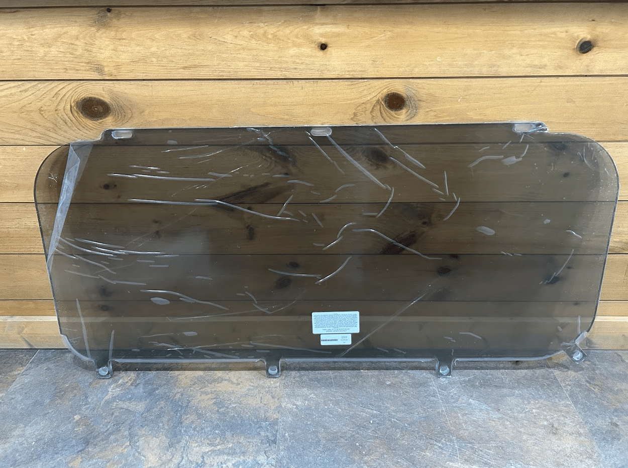 Kubota SVL tinted polycarbonate lower side window panel in protective wrap, front view against wooden background