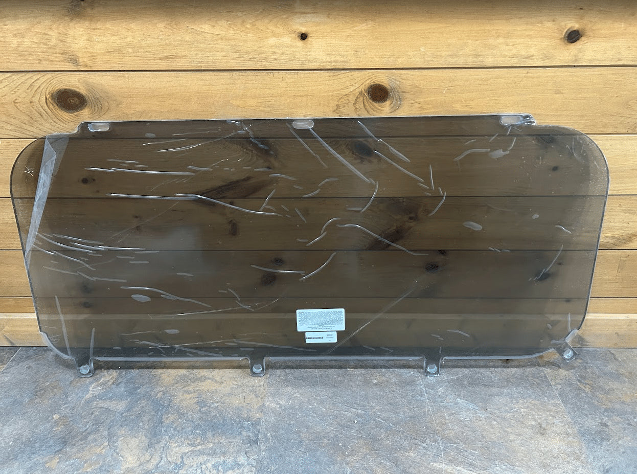 Kubota SVL tinted polycarbonate side window panel in protective wrap against wooden background, front view