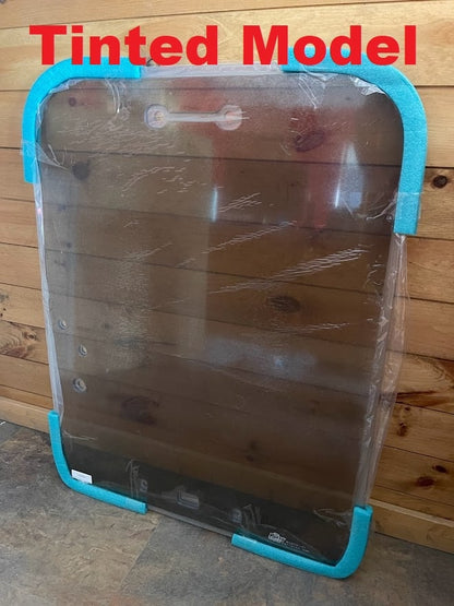 Kubota SVL tinted polycarbonate windshield in protective wrap with blue foam corners, angled view showing metal hardware