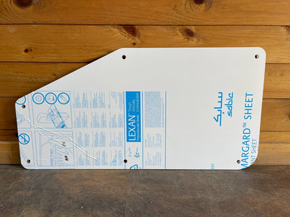 Kubota SVL upper corner polycarbonate side window panel with Lexan Margard protective film showing diagonal cut shape
