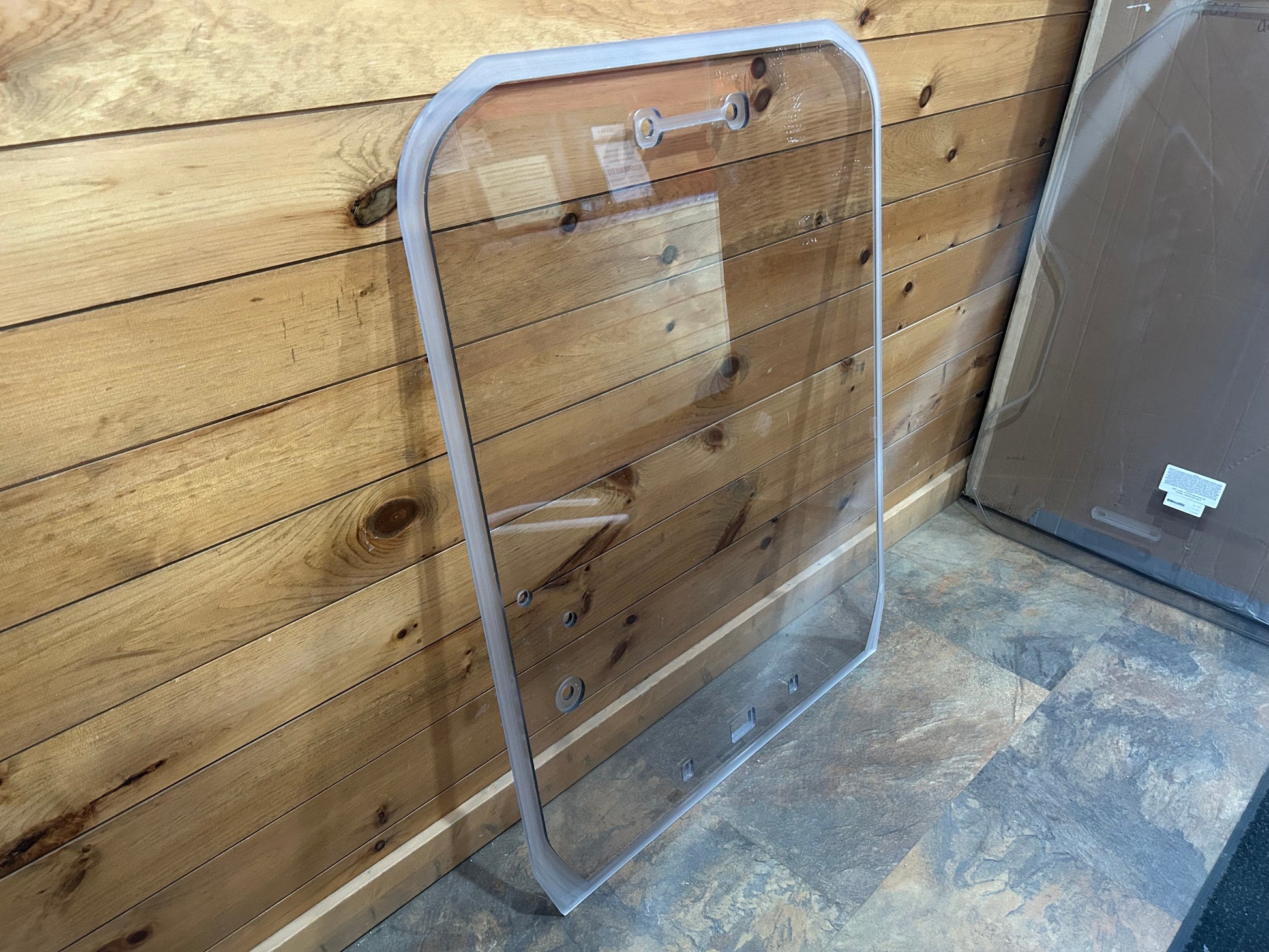 Tinted polycarbonate Kubota SVL windshield leaning against a wood wall next to another door panel