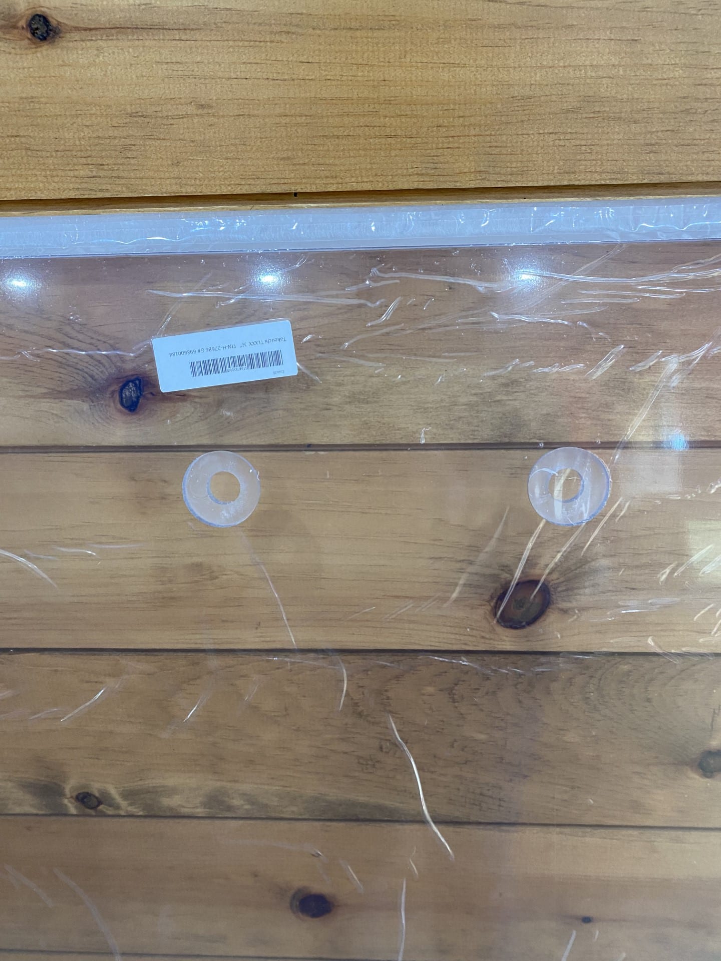 Close-up of top edge of Takeuchi TL polycarbonate windshield showing two upper mounting grommets and label sticker