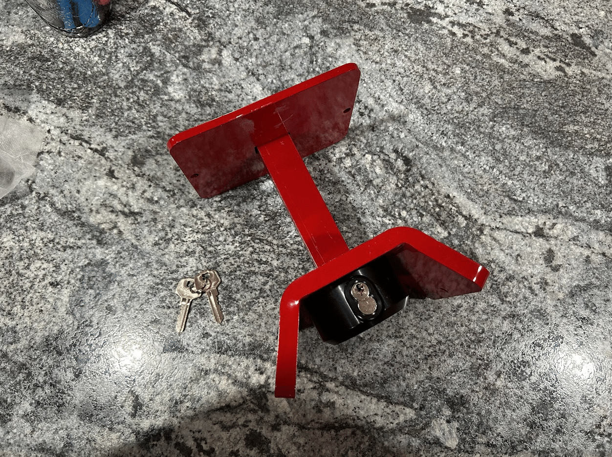 Assembled Trac-Lock anti-theft device showing red steel bracket with black lock cylinder and included keys