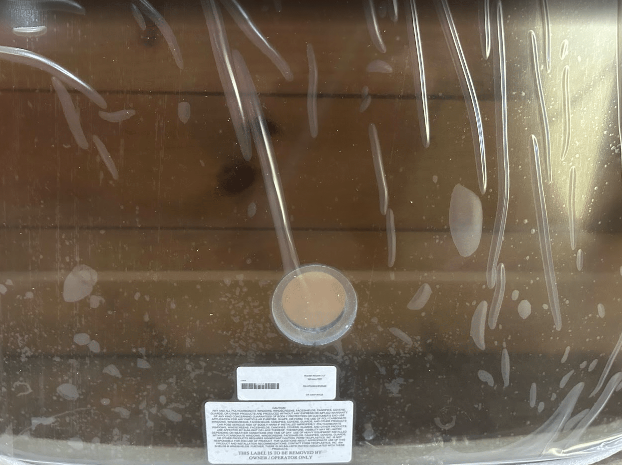 Close-up of the bottom of a Wacker Neuson ST/SW tinted windshield showing the wiper motor hole cutout and product label